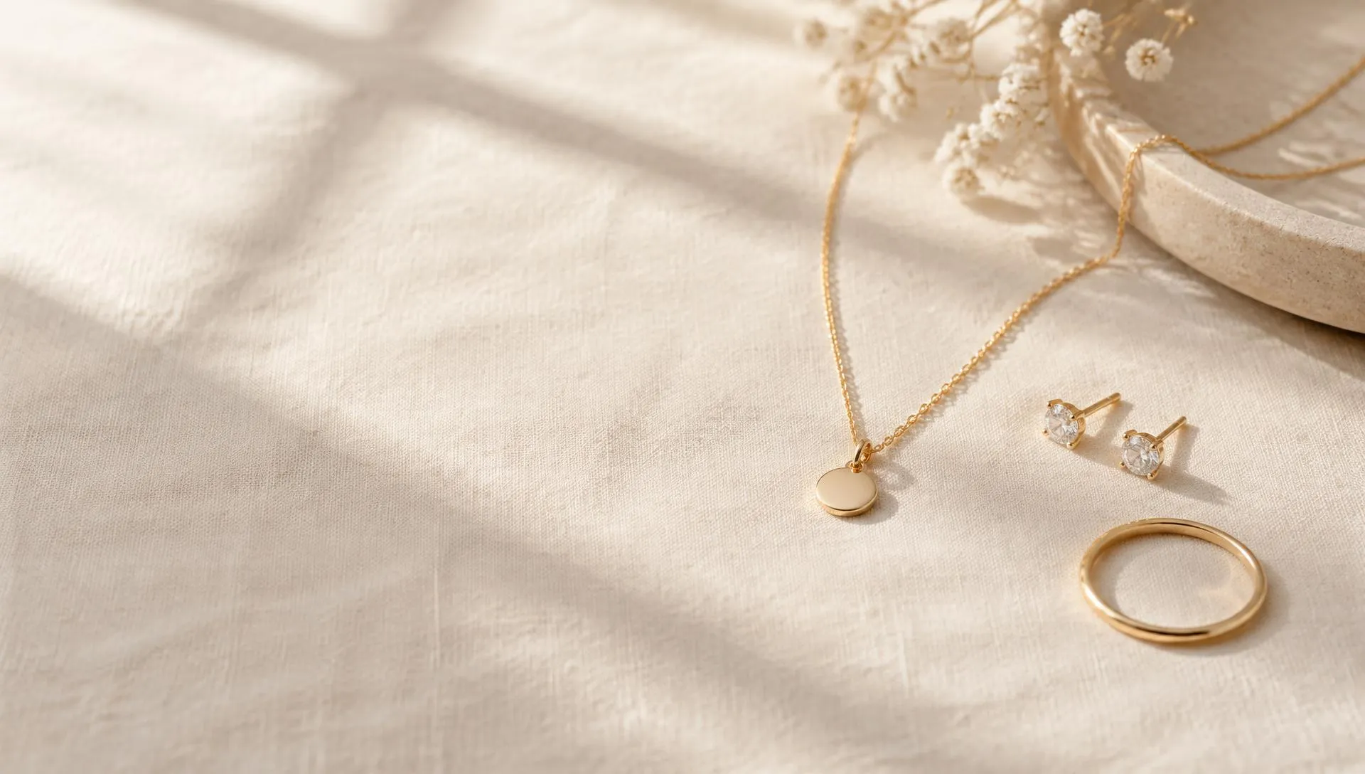 Minimal gold-tone pendant, stud earrings and ring on ivory linen